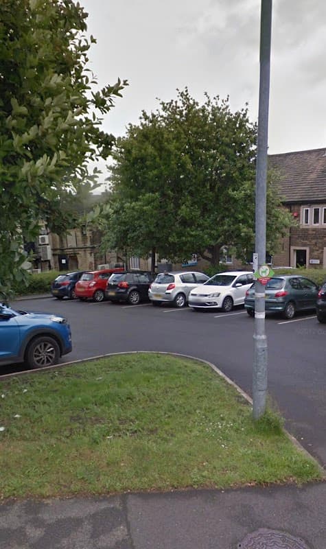 Car park with several parked cars, surrounded by greenery and buildings in Honley, Yorkshire.