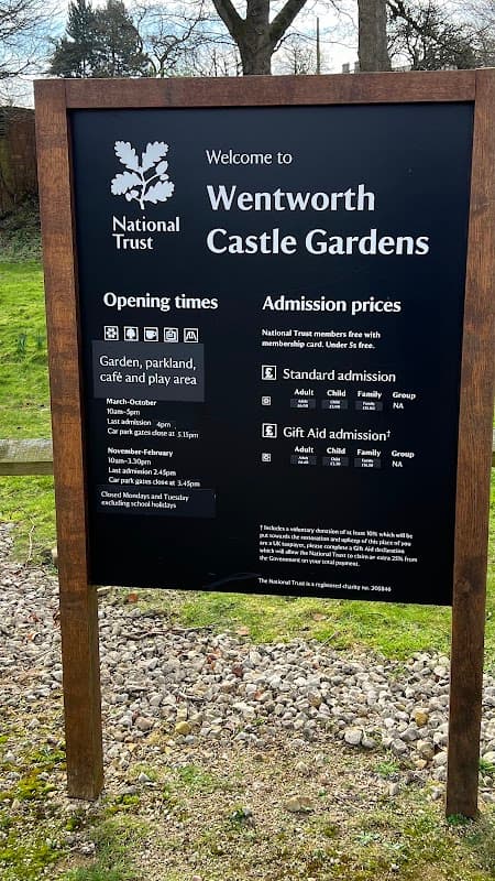 Welcome sign for Wentworth Castle Gardens, detailing opening times and admission prices, surrounded by greenery.