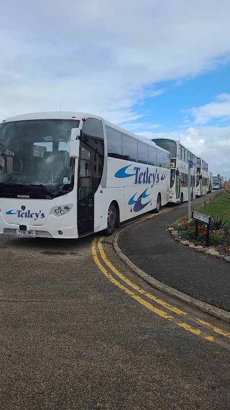 Two white coaches with "Tetley's" branding parked in a coach drop-off area, with a cloudy sky in the background.
