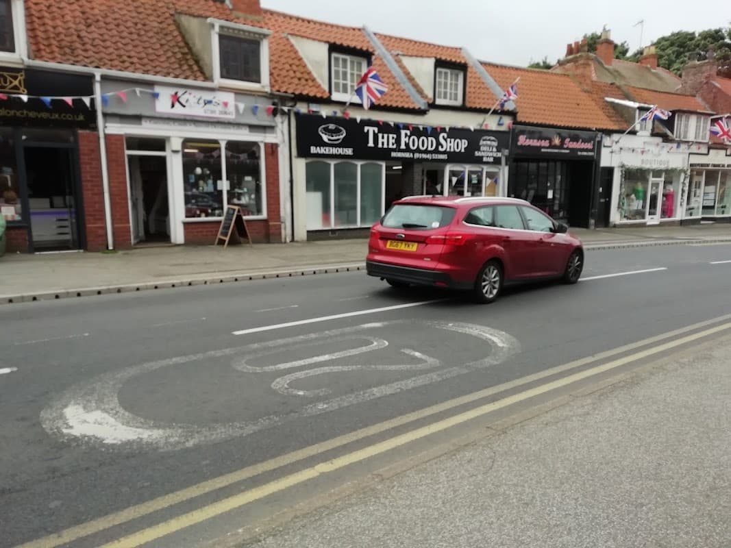 On-street parking area with a red car, shops with Union Jack flags, and a clear road in Hornsea, Yorkshire.