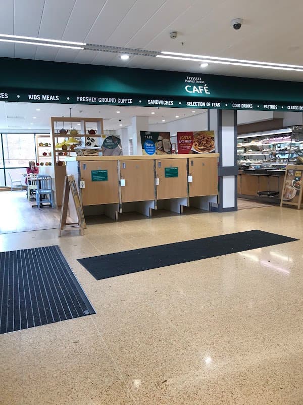 Entrance to Morrisons café with wooden counters, menu boards, and a display of pastries and drinks.