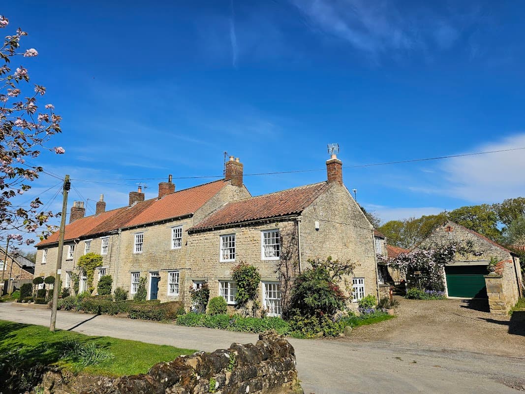 Stone cottages with red roofs, surrounded by greenery, under a clear blue sky in Hovingham, Yorkshire.