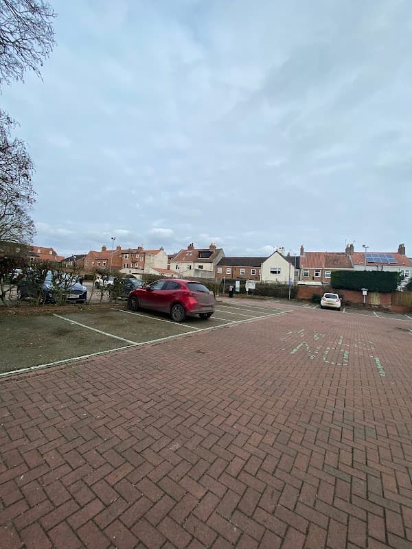Bishops Manor House car park with empty spaces and nearby buildings under a cloudy sky.