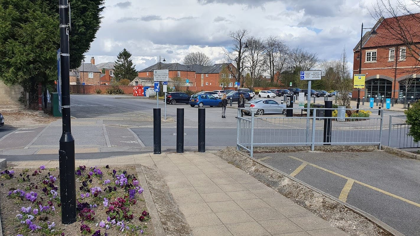 Pay & Display car park with parked cars, signage, and flower beds, set against a cloudy sky in Howden, Yorkshire.