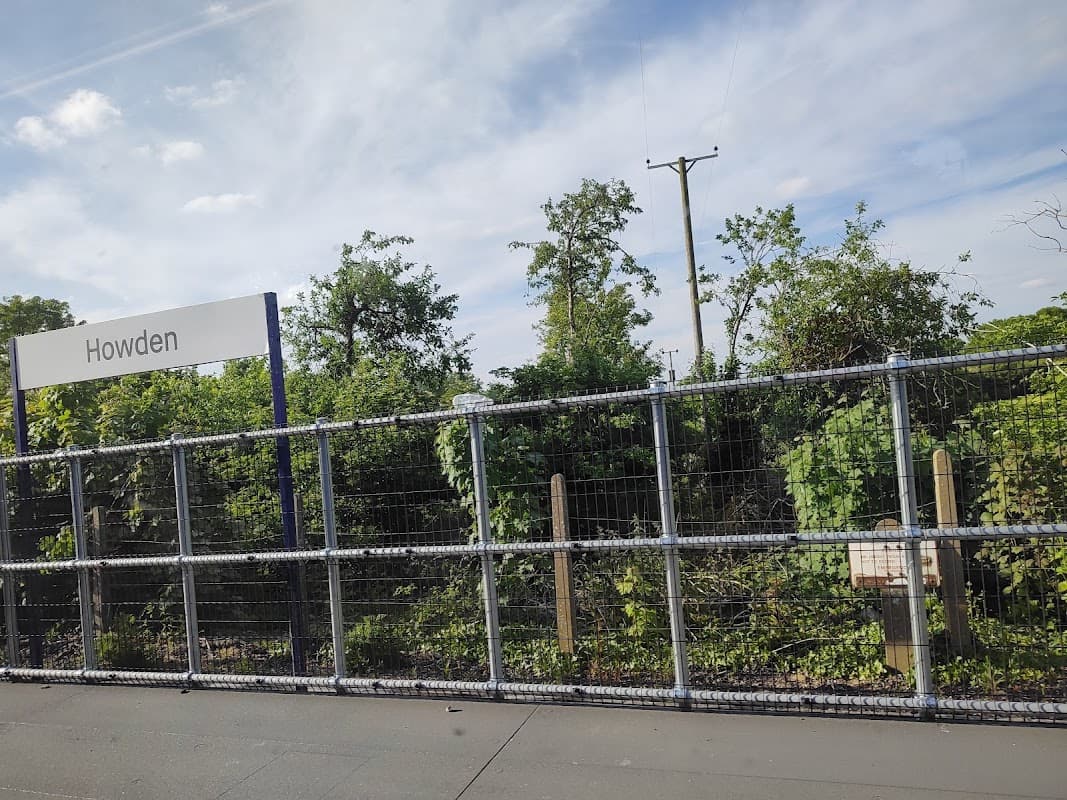 Sign for Howden with greenery and trees in the background, enclosed by a wire fence under a blue sky.