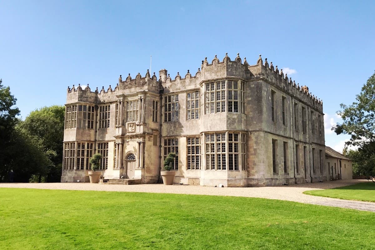 Historic Howsham Hall features ornate stone architecture, large windows, and manicured lawns under a clear blue sky.