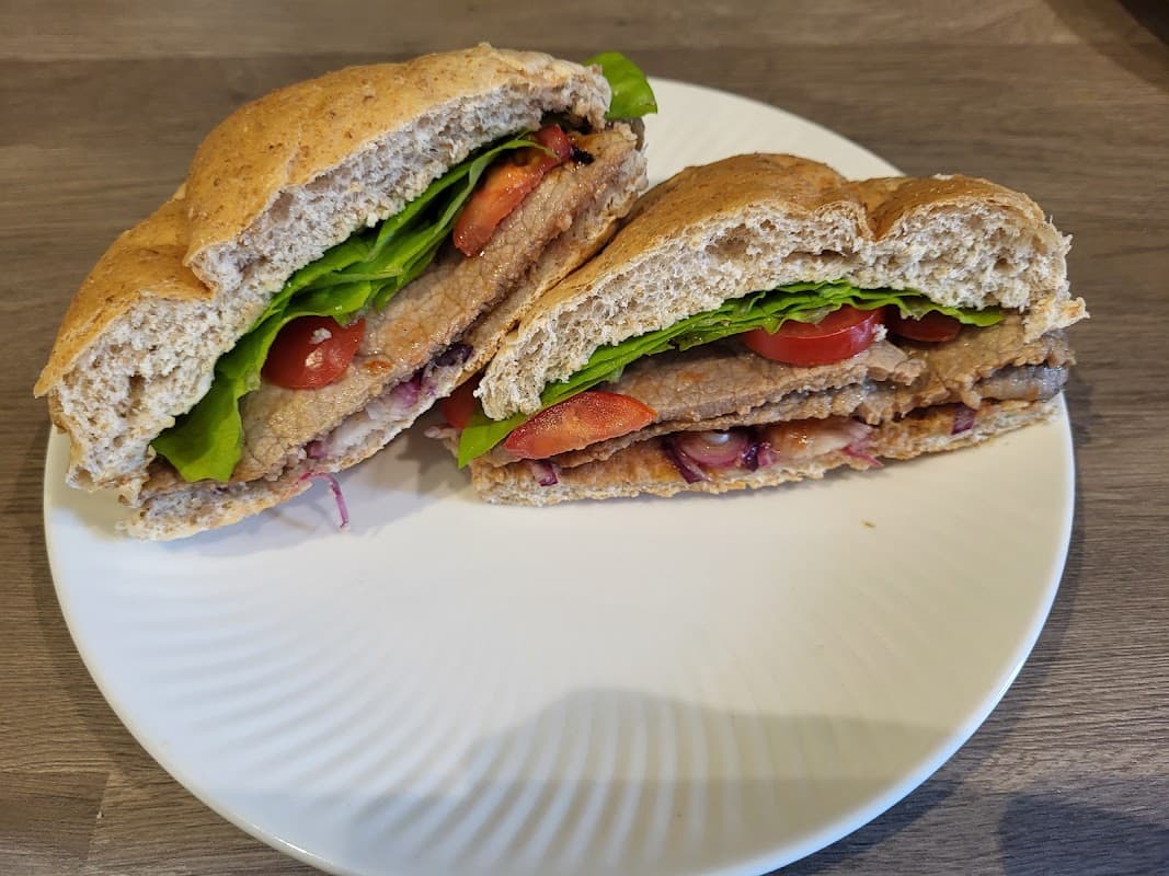 A plate with a sliced sandwich filled with lettuce, tomatoes, and a meat substitute on whole grain bread.