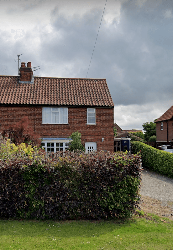 Ebor Equine Therapy building with a red-tiled roof, surrounded by greenery and a gravel driveway under a cloudy sky.