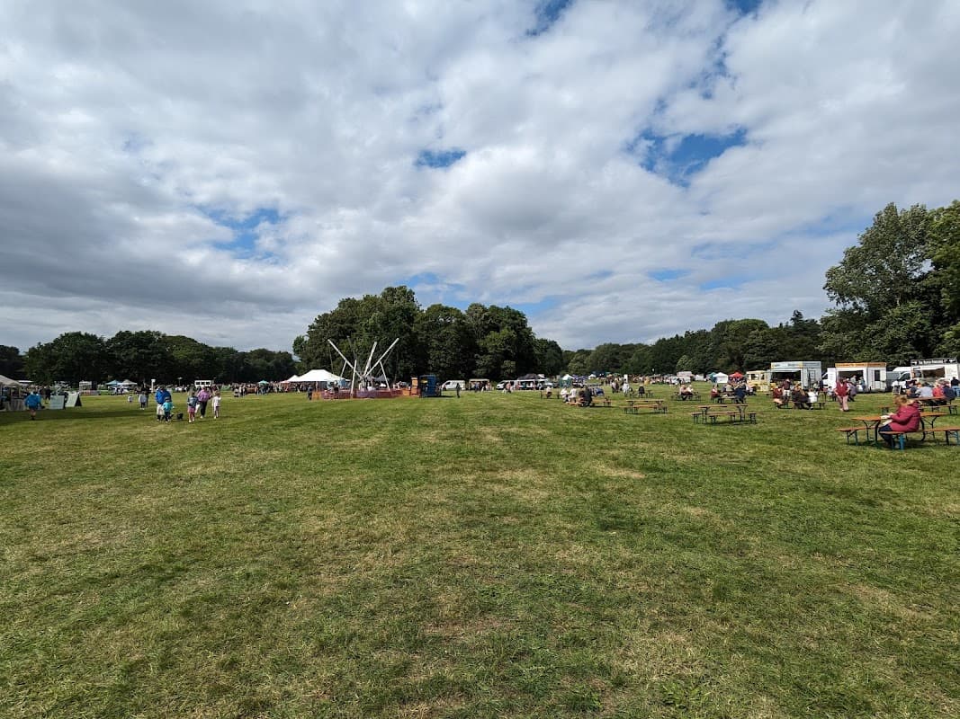 Wide view of a grassy field filled with people, tents, and food stalls under a partly cloudy sky.