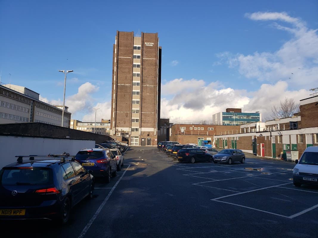Rooftop car park with parked cars, a tall building in the background, and a clear blue sky with scattered clouds.