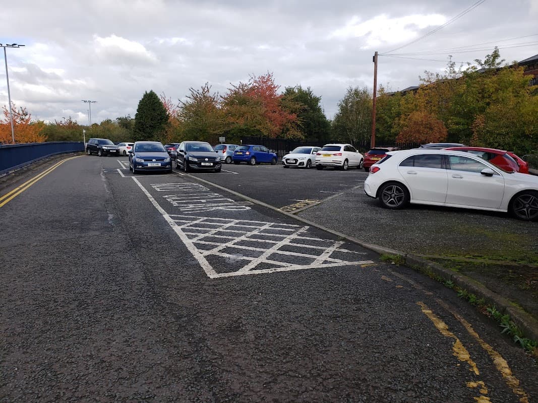 Cars parked in a spacious lot surrounded by trees with autumn foliage under a cloudy sky.