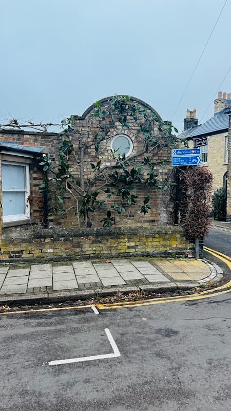 Pay & Display sign at Cambridge Road Car Park, with a stone wall and greenery, near a residential street.