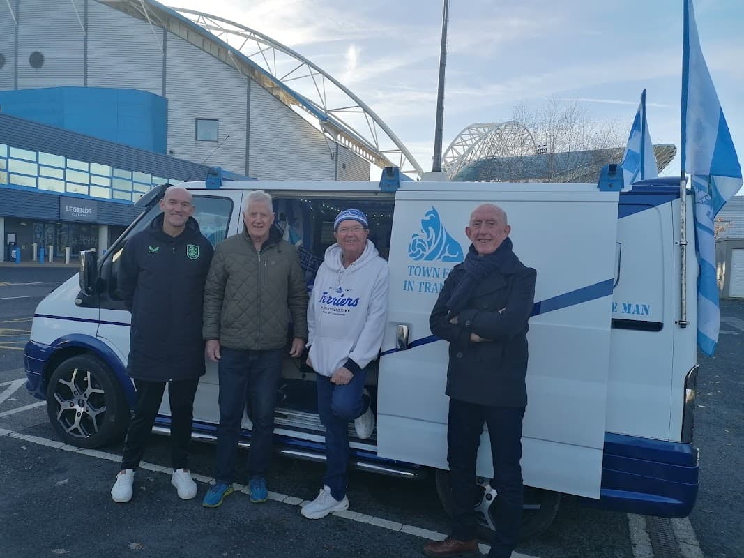 Four men stand next to a van decorated with flags in a car park near a stadium in Huddersfield, Yorkshire.