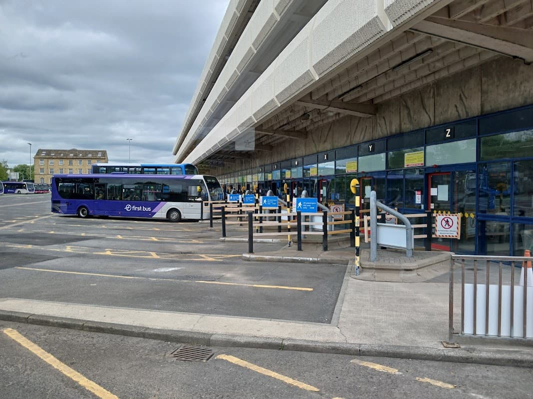 Pay & Display car park at Huddersfield Bus Station with buses, signage, and parking barriers under a cloudy sky.