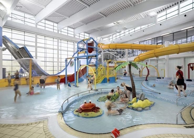 Indoor water park featuring slides, pools, and families enjoying the facilities under large windows.