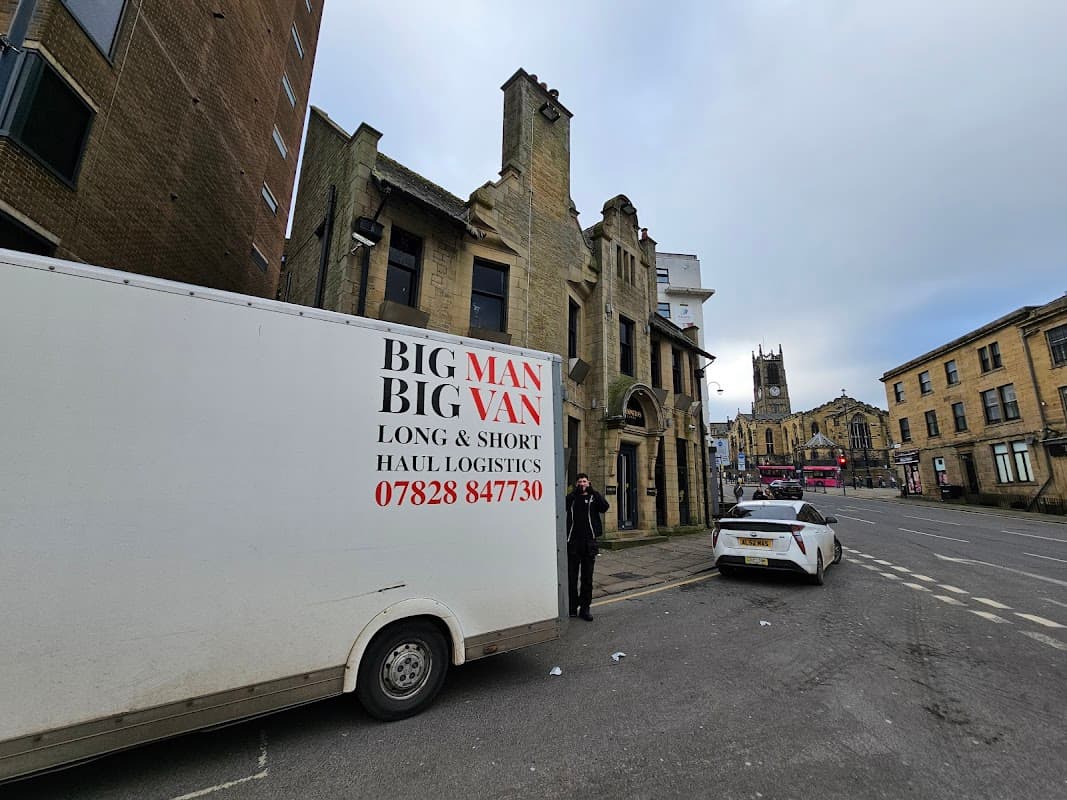 Kingsgate Parking area with a logistics van, historic buildings, and a church tower in Huddersfield, Yorkshire.