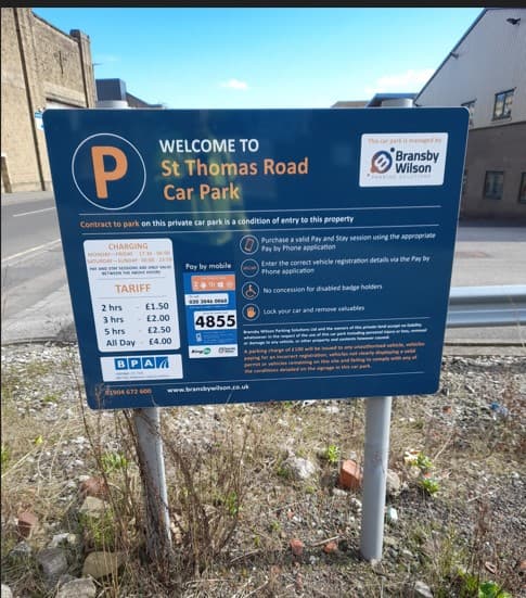 Welcome sign for St Thomas Road Car Park with parking tariffs and instructions for payment displayed on a blue board.