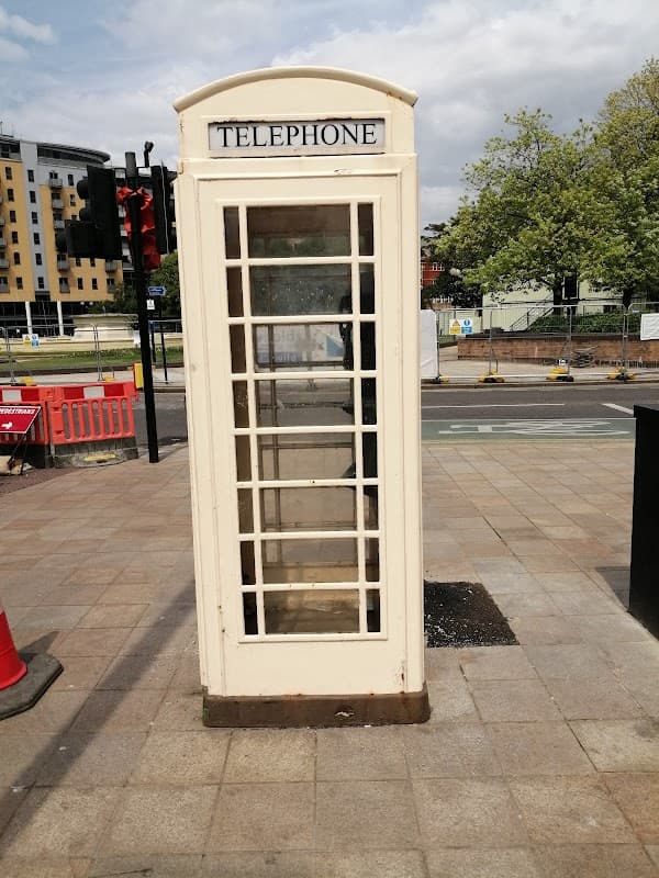 A vintage telephone booth stands on a sidewalk near a traffic signal and modern buildings in Hull, Yorkshire.