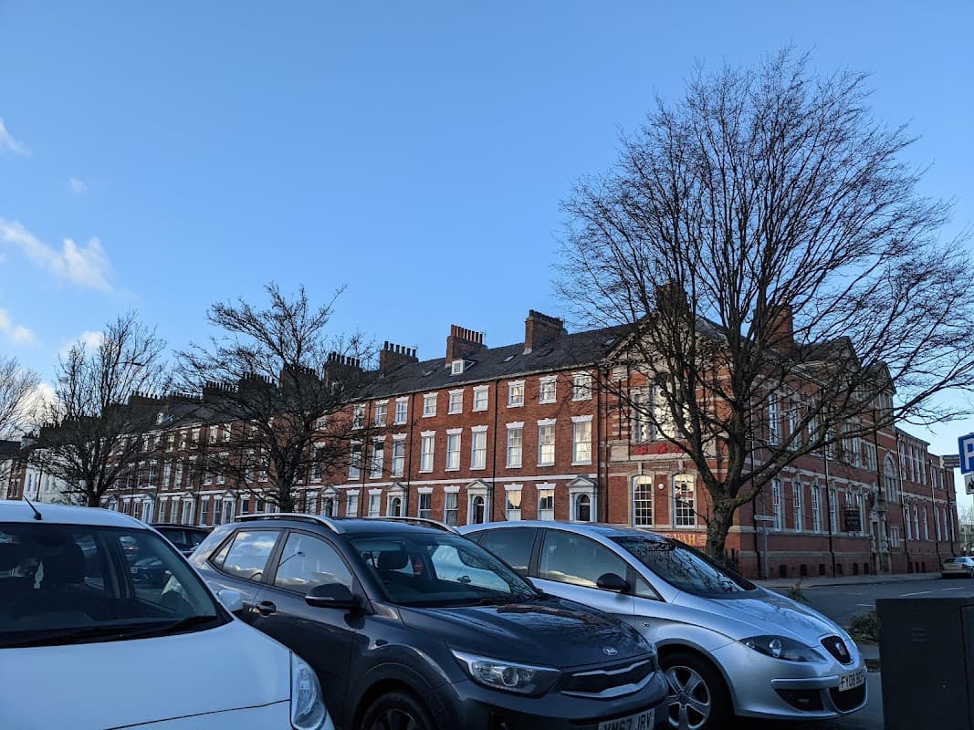 Row of red-brick buildings under a clear blue sky, with parked cars in the foreground and bare trees nearby.
