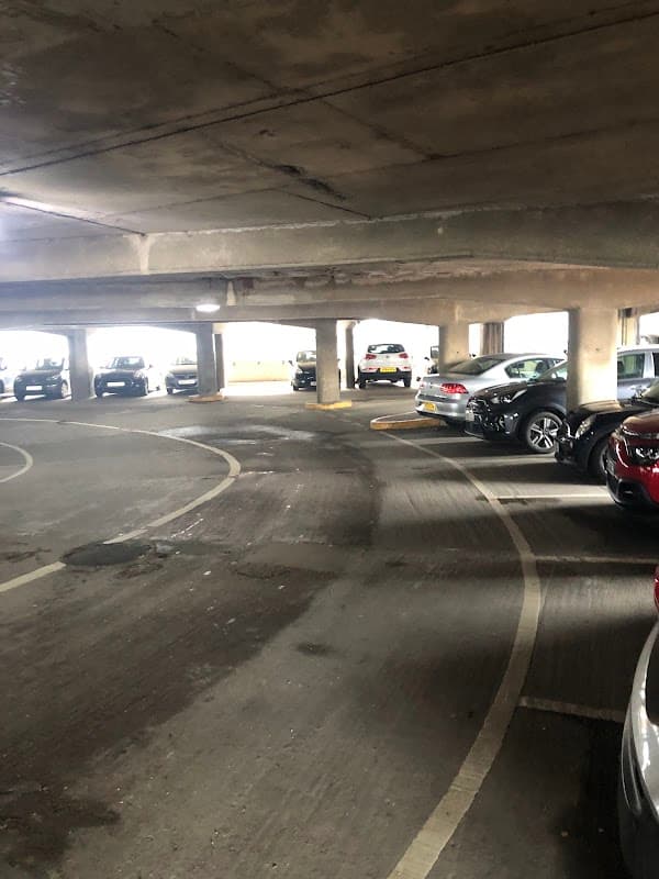 Multi-storey car park interior with parked cars and concrete pillars, featuring a winding driving path.