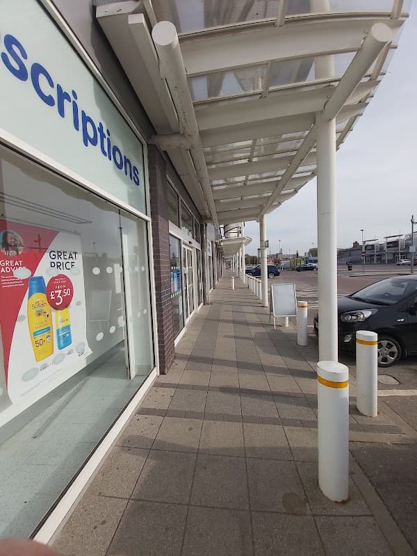 Sidewalk view of Kingston Retail Park with shops, a clear sky, and parked cars.