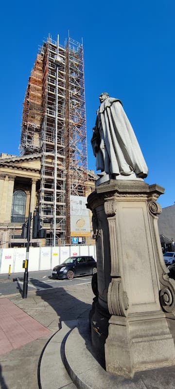 Statue on a pedestal in foreground with scaffolding and construction behind, clear blue sky above.