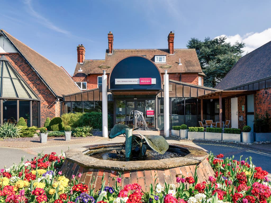 Elegant brick facade of Mercure Royal Hotel with a fountain and vibrant flower beds in the foreground.