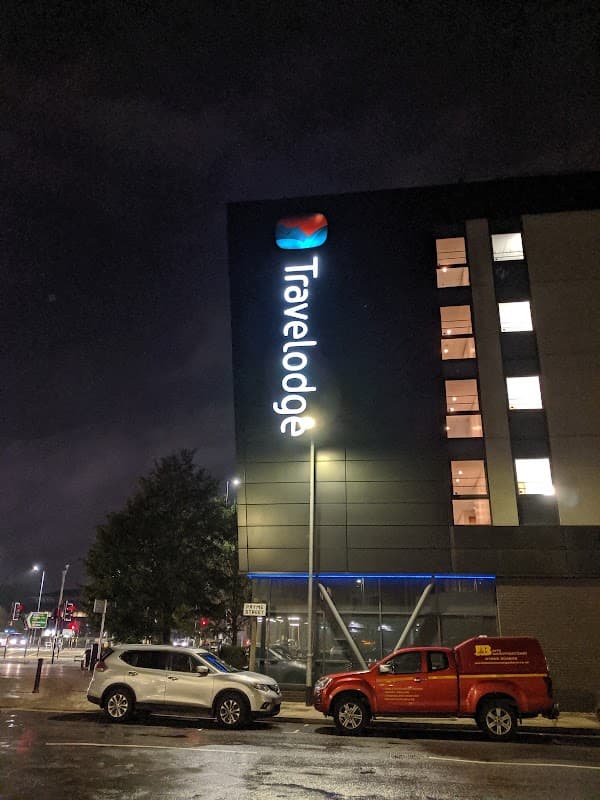 Travelodge sign illuminated at night, with parked vehicles and a wet road reflecting lights in Hull, Yorkshire.