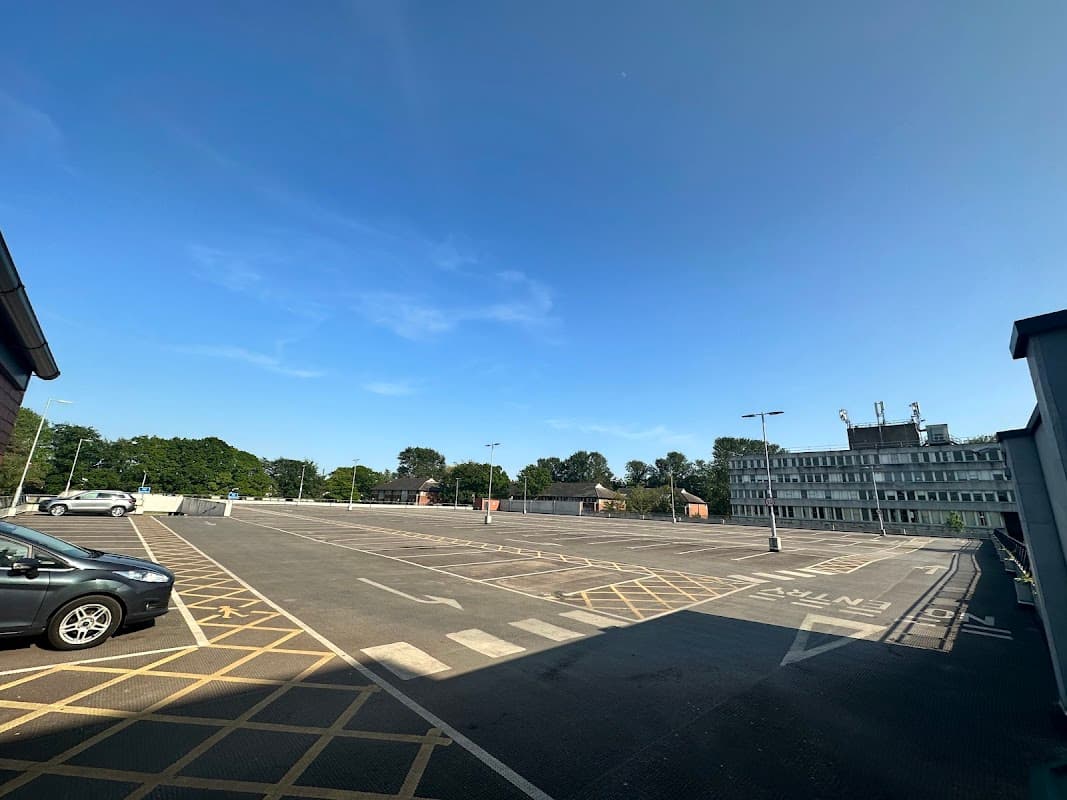 Spacious car park with clear blue sky, marked parking spaces, and a modern building in the background.