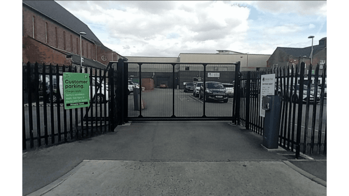 Entrance gate to a parking lot with signs for customer parking and a pay & display machine visible.