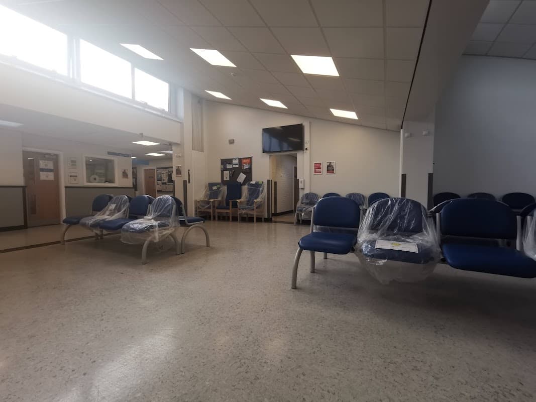 Spacious waiting area with blue chairs, a TV, and a reception desk in Hunslet Health Centre.