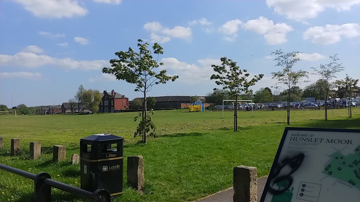 Sunny park scene with green grass, trees, a playground, and distant buildings in Hunslet, Yorkshire.