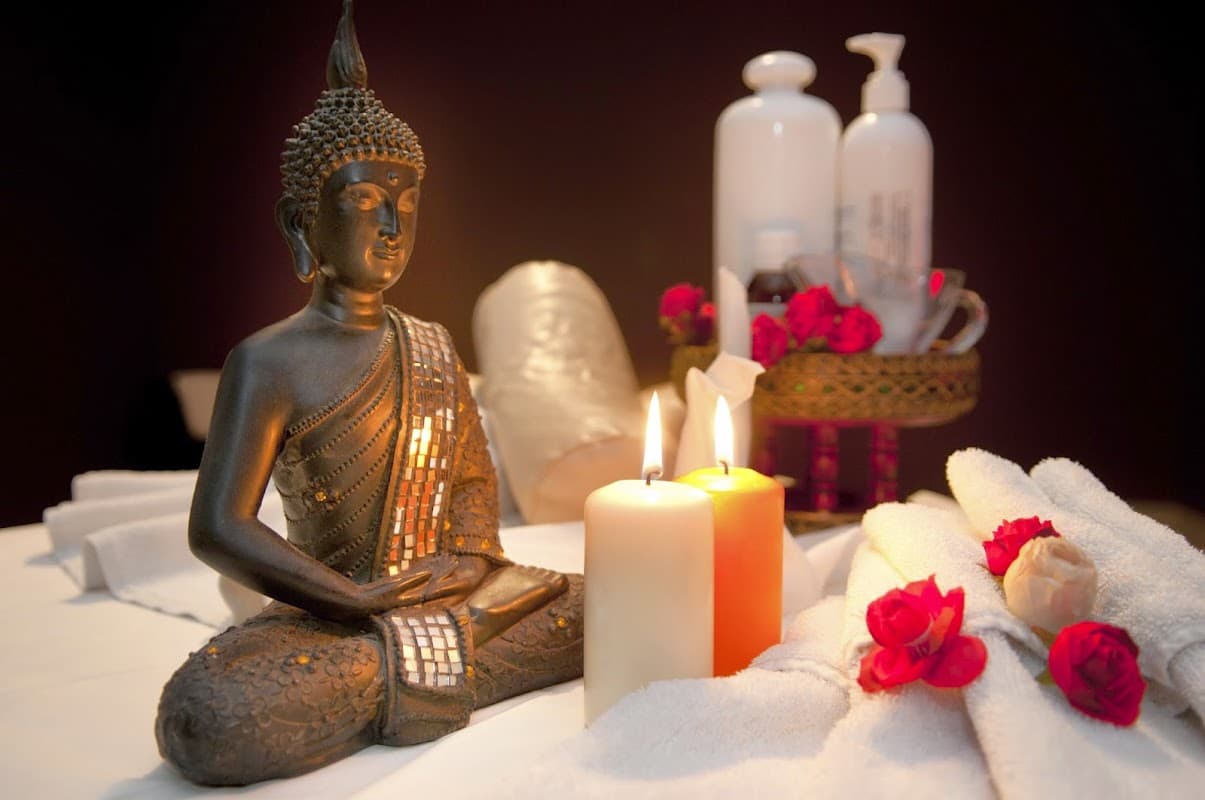 Buddha statue surrounded by candles, towels, and rose petals, creating a tranquil spa atmosphere.