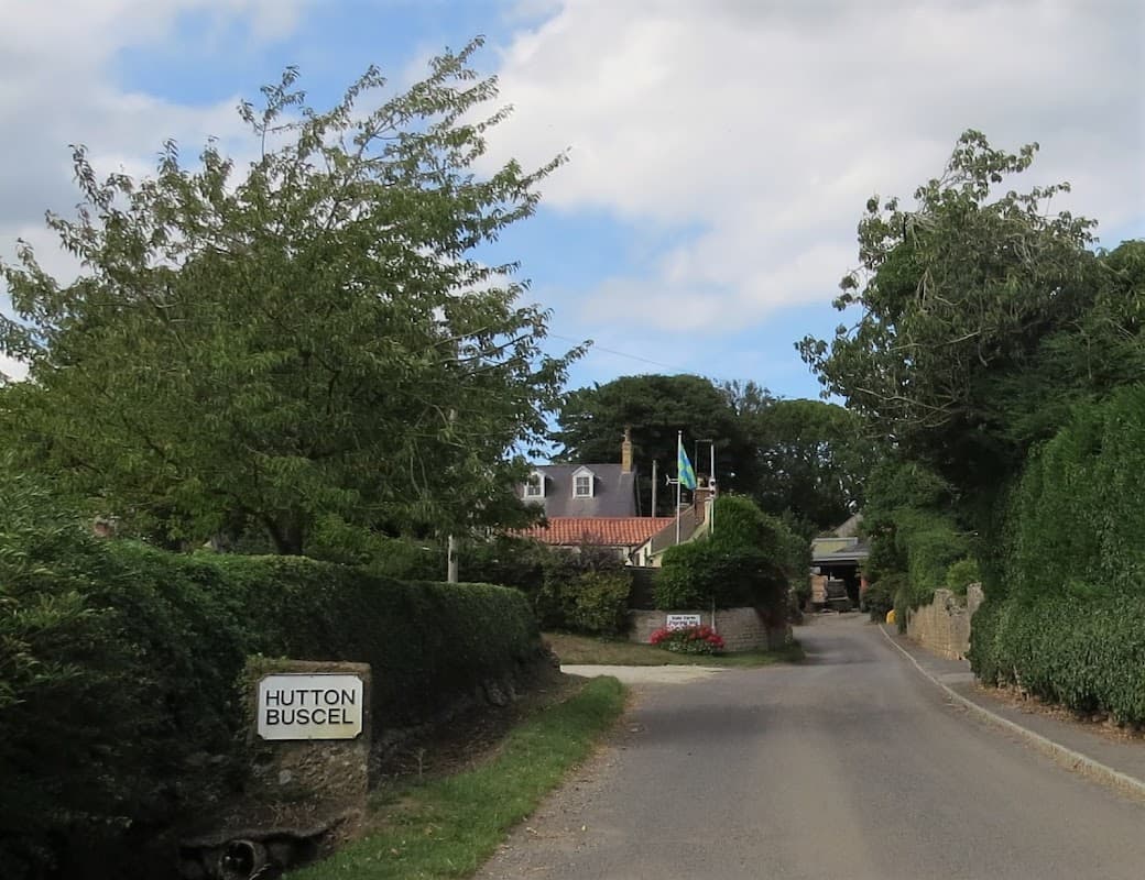 Entrance to Dale Farm Touring Park, with trees lining the road and a sign for Hutton Buscel visible.