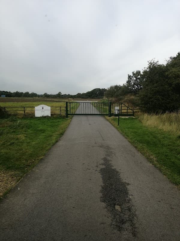 A gated entrance to Athelstan Business Park, with a gravel path leading through grassy fields under a cloudy sky.