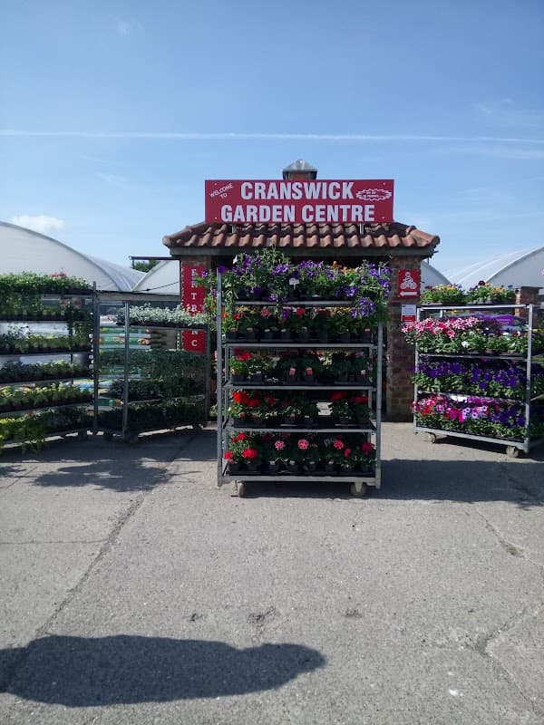 Entrance to Cranswick Garden Centre featuring colorful flower displays and a sign above. Bright blue sky in the background.