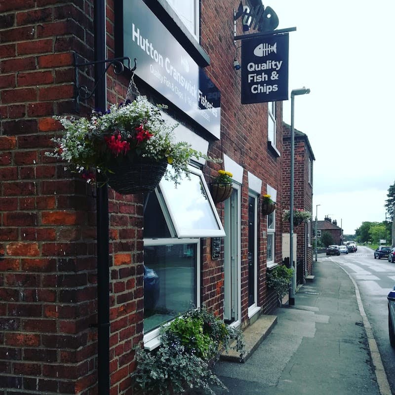 Takeaway shop with a sign for "Quality Fish & Chips," adorned with flower baskets and a brick facade in Hutton Cranswick.