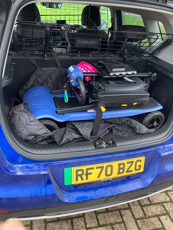 Blue vehicle trunk with a compact mobility scooter secured and covered in a quilted blanket.