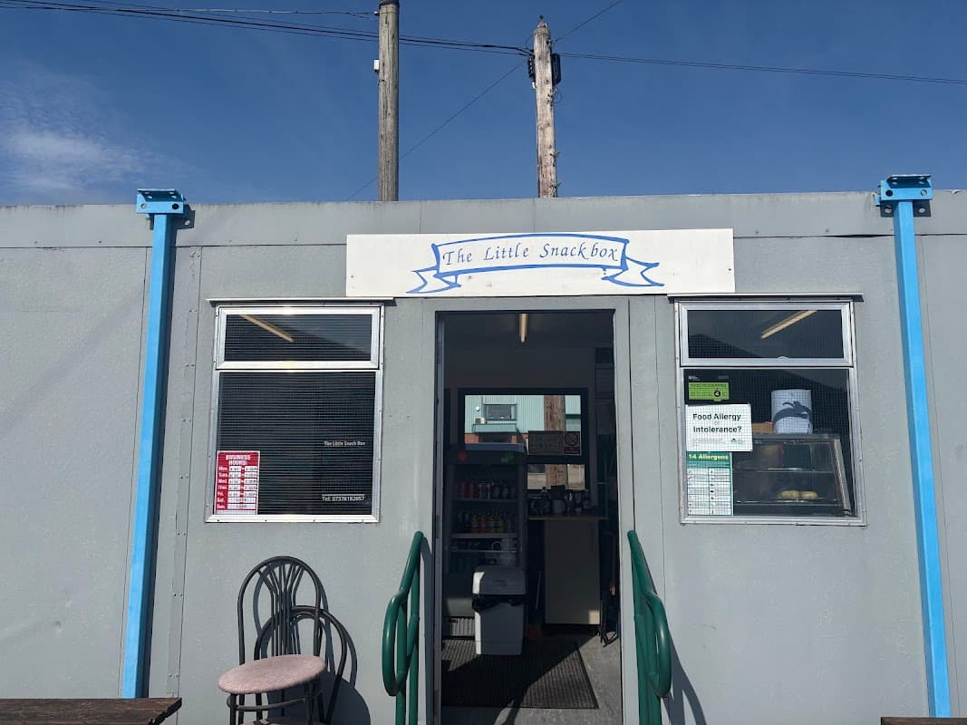 Gray building with blue accents, sign reading "The Little Snackbox," and entrance with a menu displayed.