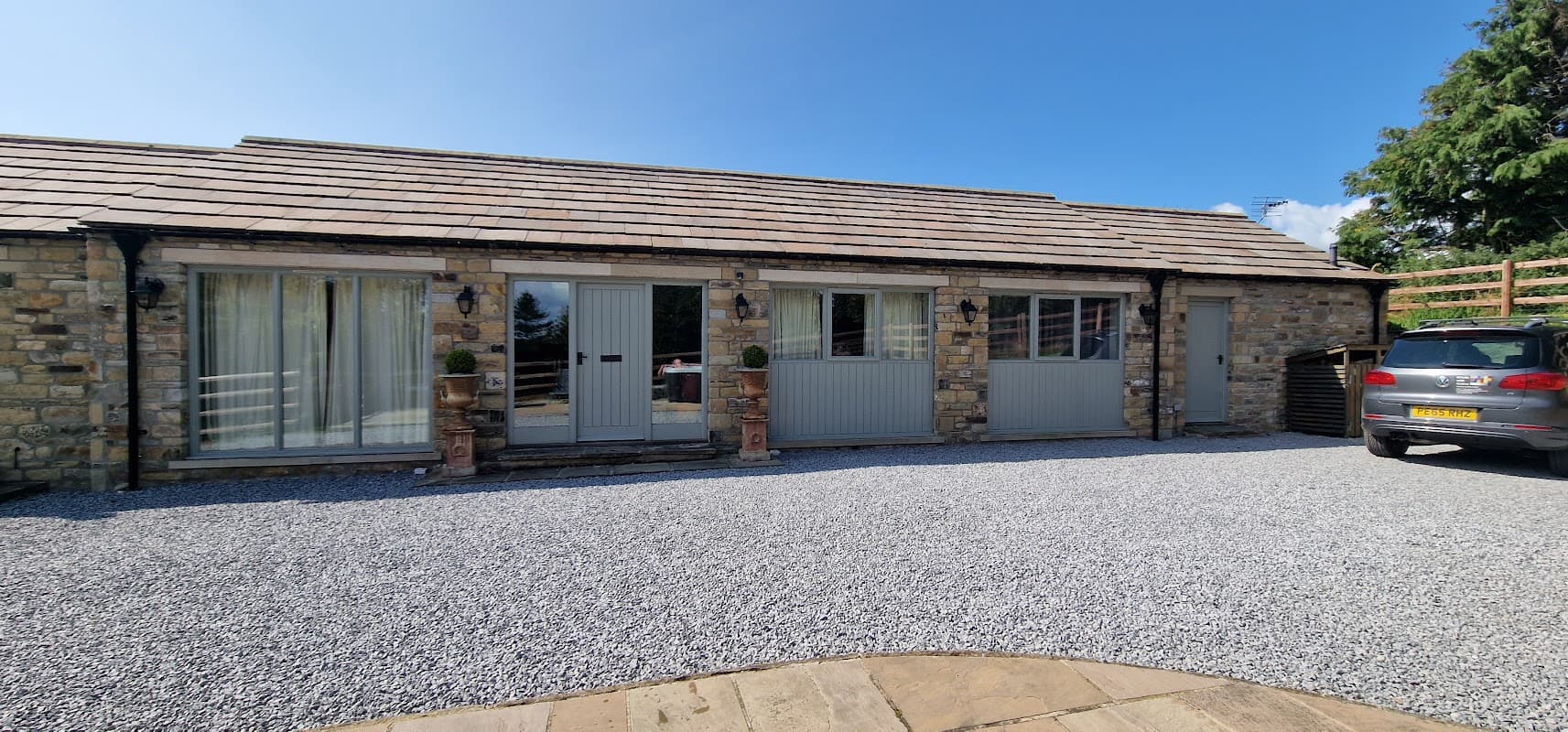 Stone building with grey doors, large windows, and a gravel driveway, surrounded by greenery in Hutton Hang, Yorkshire.