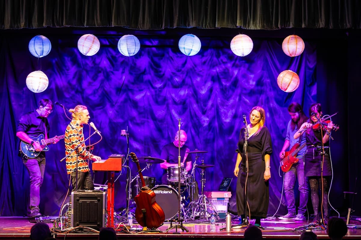 A lively performance on stage with musicians, instruments, and colorful lanterns against a purple backdrop.