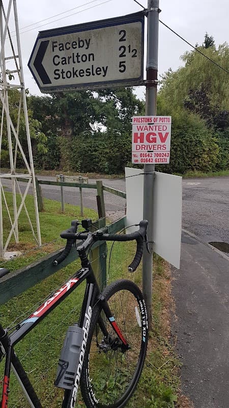 Signpost indicating directions to Faceby, Carlton, and Stokesley, with a "Wanted HGV Drivers" notice from Prestons of Potto.