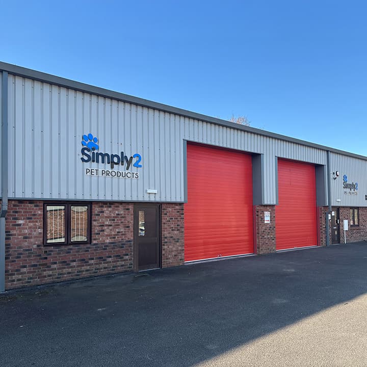 Exterior of Simply2 Pet Products with red garage doors, brick facade, and clear blue sky above.