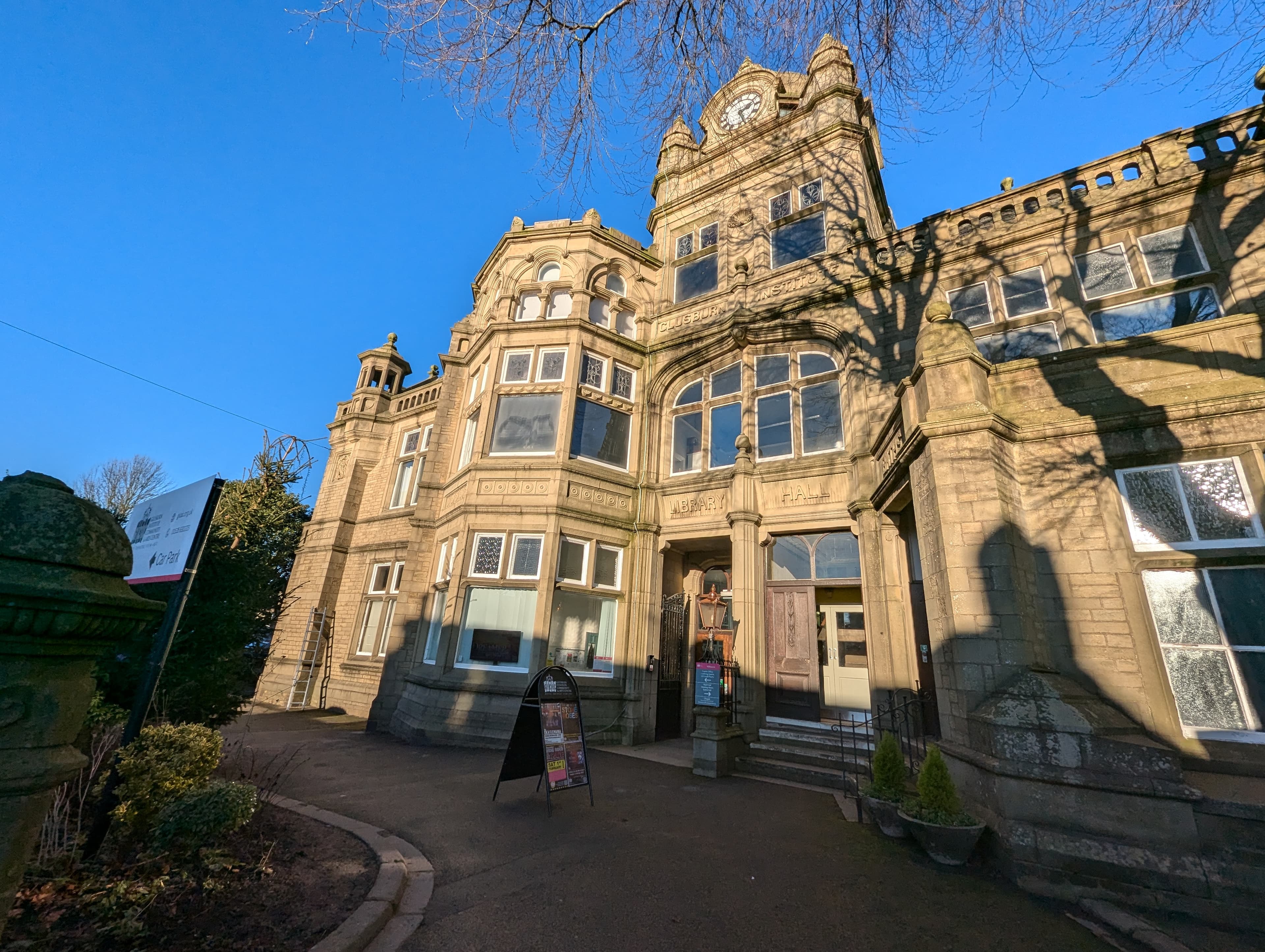 Victorian-style building with ornate stonework and a clock tower, featuring a sign for Glusburn Institute.