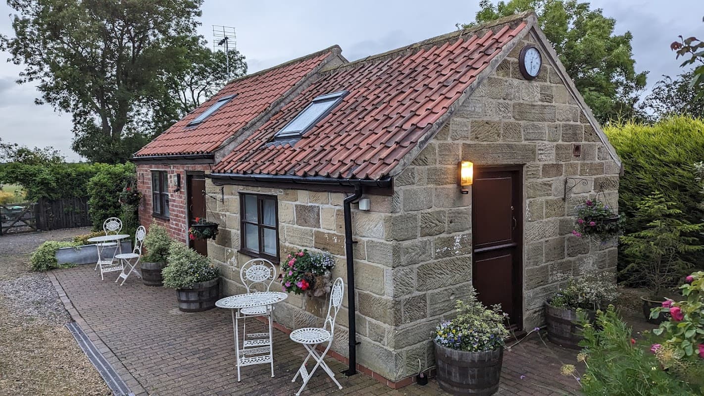 Charming stone cottage with red-tiled roof, garden seating, and flower pots in a rural Yorkshire setting.