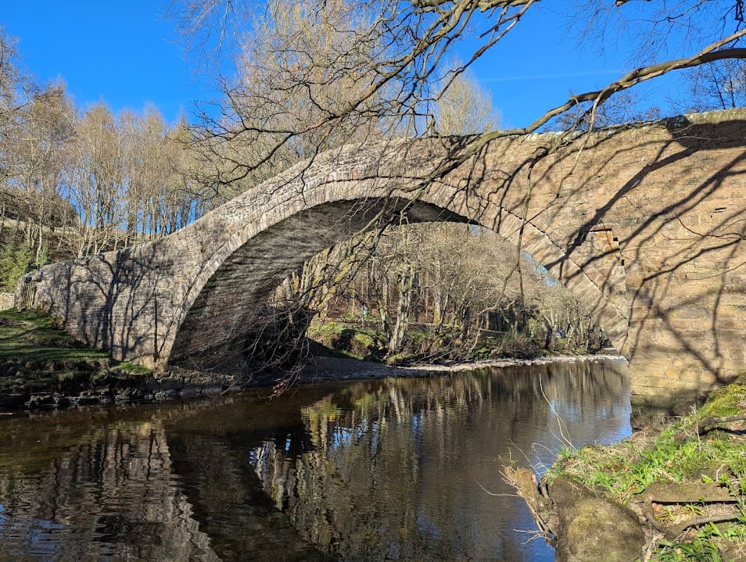 Stone arch bridge over a calm river, surrounded by bare trees and a clear blue sky.