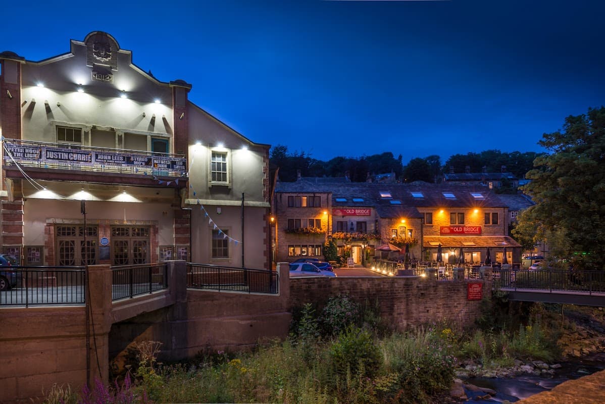 The Old Bridge Inn lit up at night, with outdoor seating and a flowing river nearby.