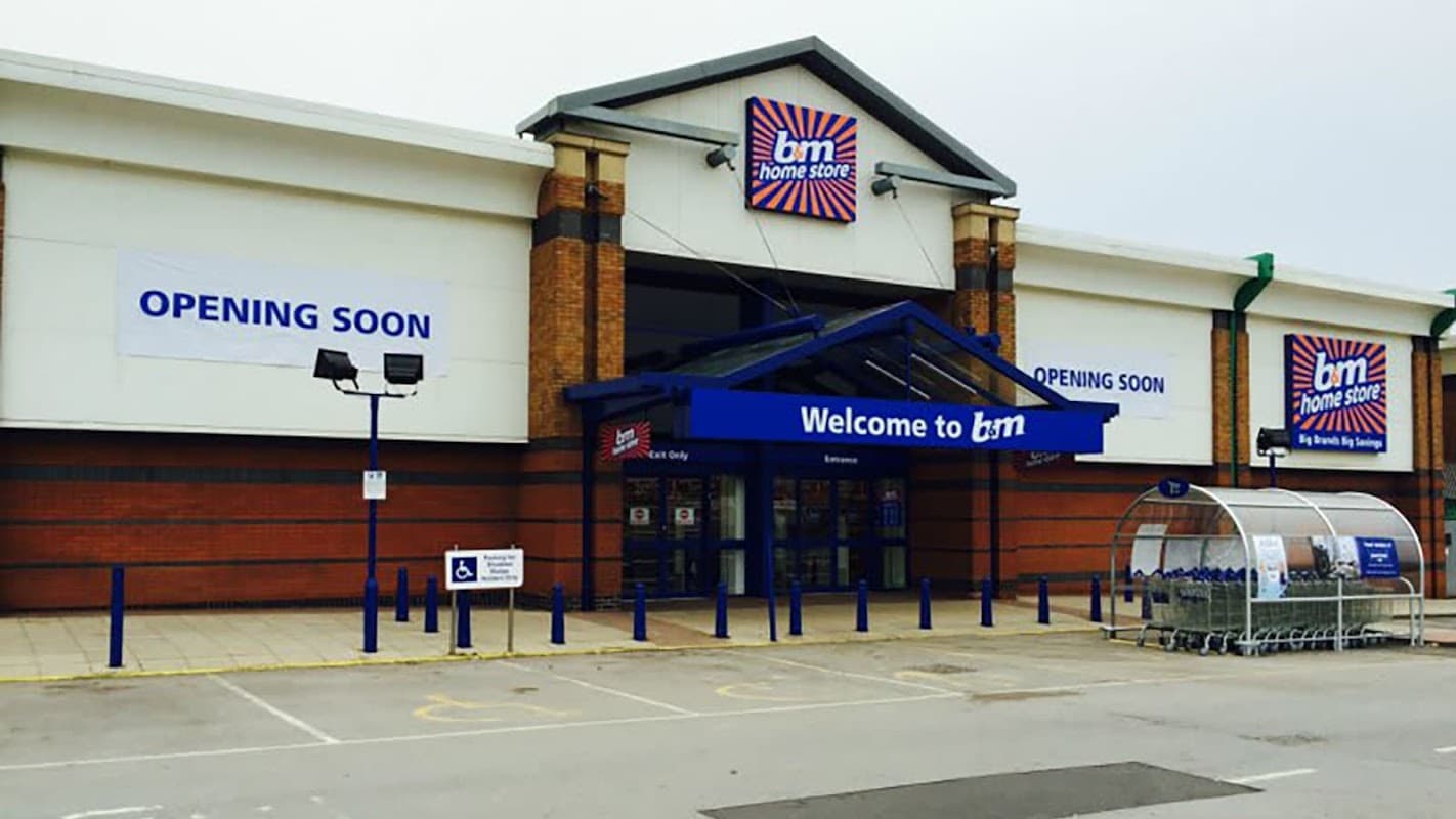 B&M Home Store entrance with a blue canopy, "Opening Soon" signs, and a trolley bay in front.