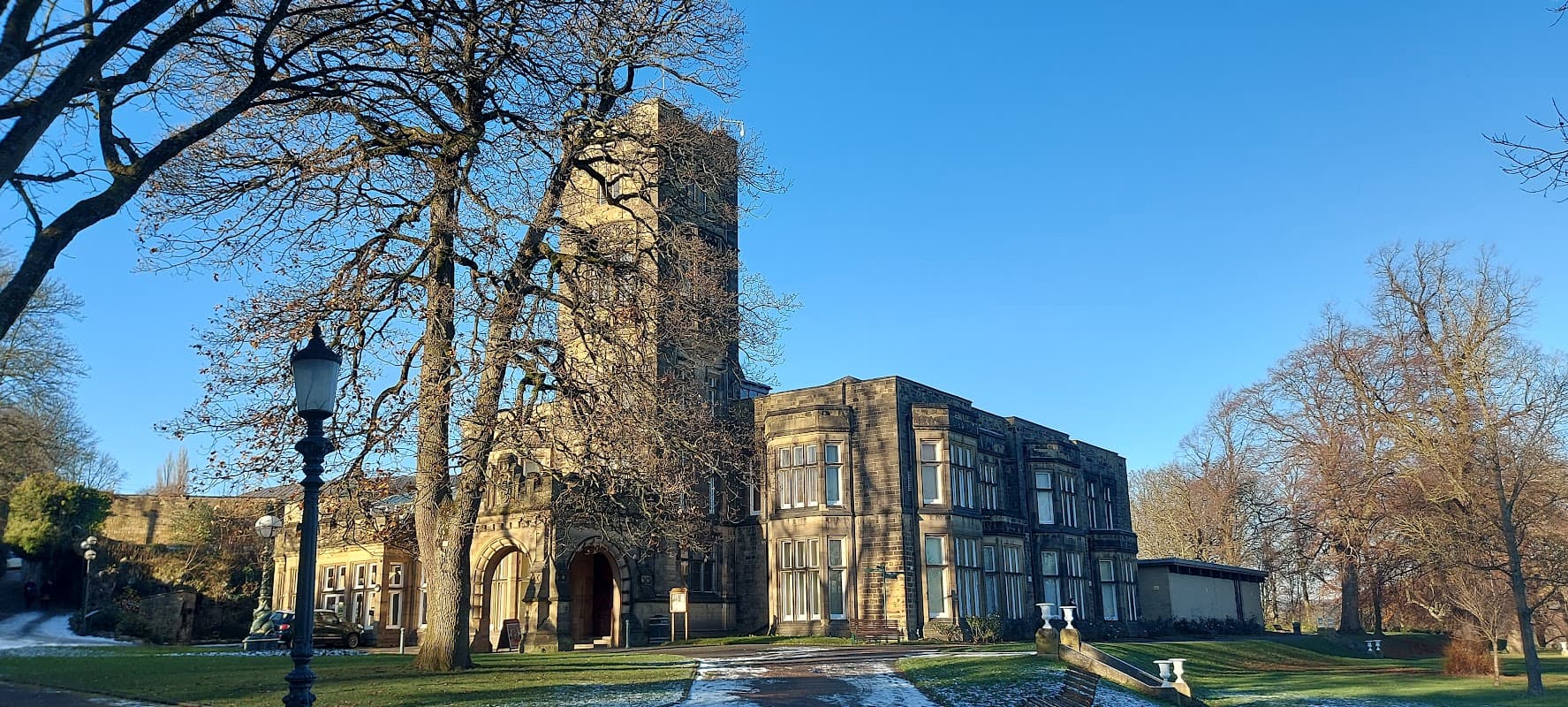 Historic Cliffe Castle with stone architecture, surrounded by trees and clear blue sky, near a car park.