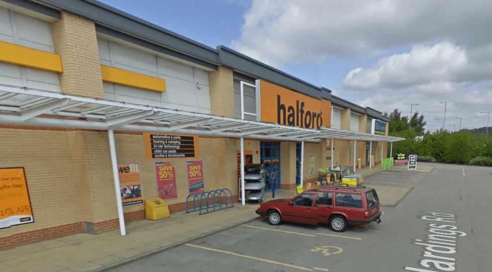 Halfords store exterior in Keighley, featuring bike racks, promotional signage, and a parked red vehicle.